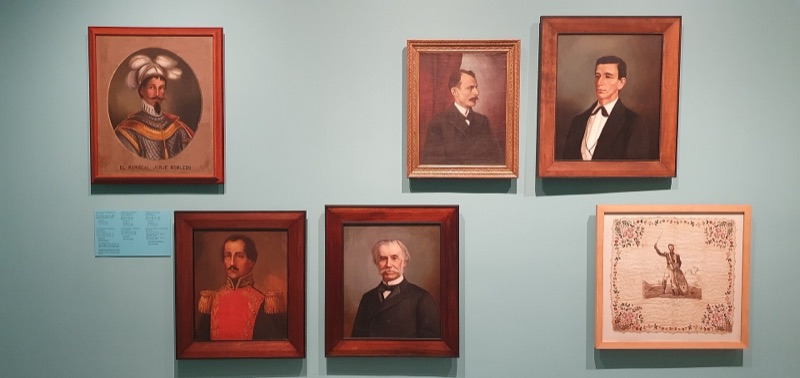Nineteenth-century portrait paintings in wooden frames on a pale blue wall at the Museo de Antioquia