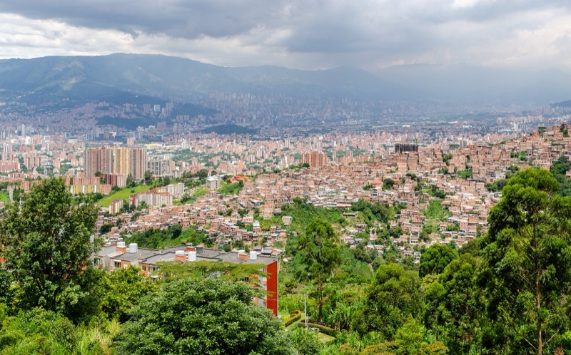 View over Medellín's Aburrá Valley from the western hills, with brick neighborhoods in front and high-rises and mountains beyond